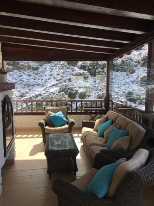 Glazed terrace at Hotel Mulhacén Trevélez with beige seating, turquoise pillows, and snowy mountain views from Granada, Spain