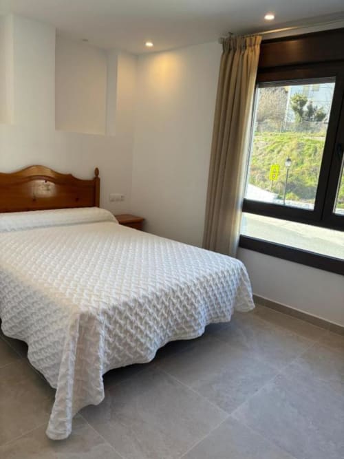 Acogedora habitación doble del Hotel Mulhacén Trevélez con vistas al río, cama de madera, cortinas beige y vistas al paisaje montañoso