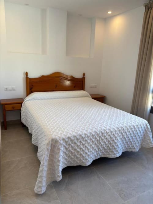 Bedroom at Hotel Mulhacén Trevélez featuring wooden bed with white bedspread and nightstand in Granada