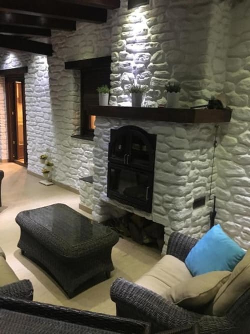 Modern apartment lounge with white stone fireplace, black wood stove, gray seating, and blue cushions at Hotel Mulhacén