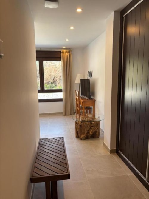 Pasillo moderno del Hotel Mulhacén con banco de madera, mesa con plantas, puertas de madera oscura y ventana con vista al río