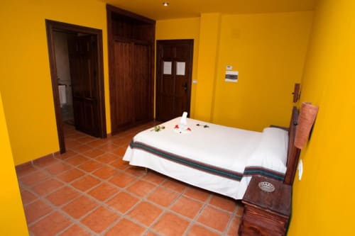 Dormitorio amarillo brillante con baldosas de barro, cama de madera con sábanas blancas y puertas de madera oscura en Hotel Mulhacén Trevélez