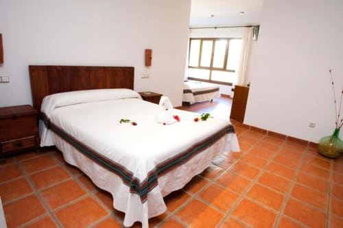 Dormitorio espacioso en Hotel Mulhacén Trevélez con cama de madera, sábanas blancas, piso de barro y vistas a las montañas