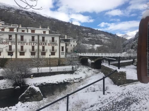 Hotel Mulhacén Trevélez snow-covered courtyard with bridge, stream, and Sierra Nevada mountains in Granada, Spain