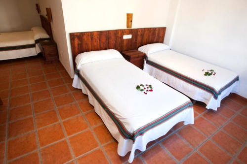 Dos camas individuales con sábanas blancas y cenefas coloridas en amplia habitación del Hotel Mulhacén Trevélez, con suelo de barro