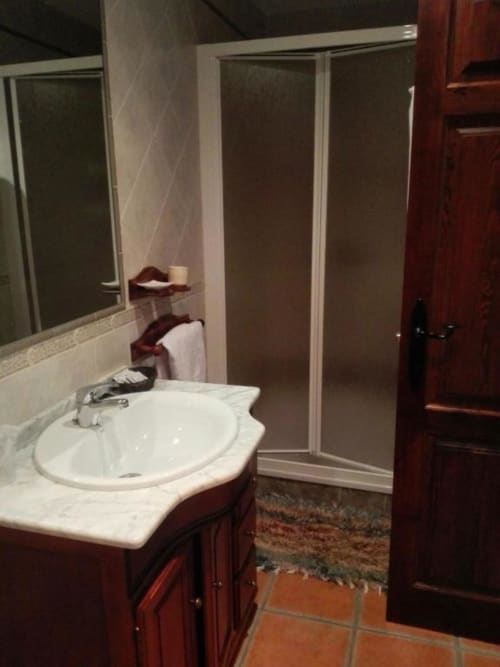 Baño moderno con lavamanos circular blanco, encimera de mármol, muebles de madera oscura y ducha de cristal en Hotel Mulhacén
