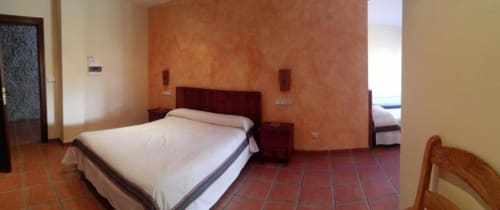 Amplia sala familiar del Hotel Mulhacén Trevélez con paredes de terracota, cama queen y vistas a la montaña