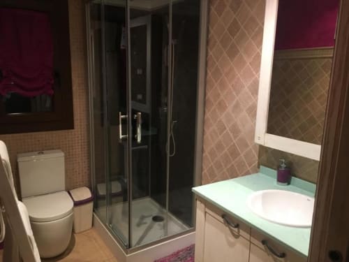 Modern bathroom at Hotel Mulhacén Trevélez with glass shower enclosure, white sink vanity, toilet, and beige tiled walls with