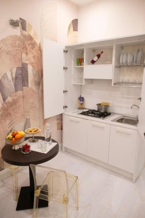 Moderna kitchenette bianca in Exclusive Domus Gaudia Roma con piano cottura, lavandino, tavolo da pranzo e opera d'arte astratta