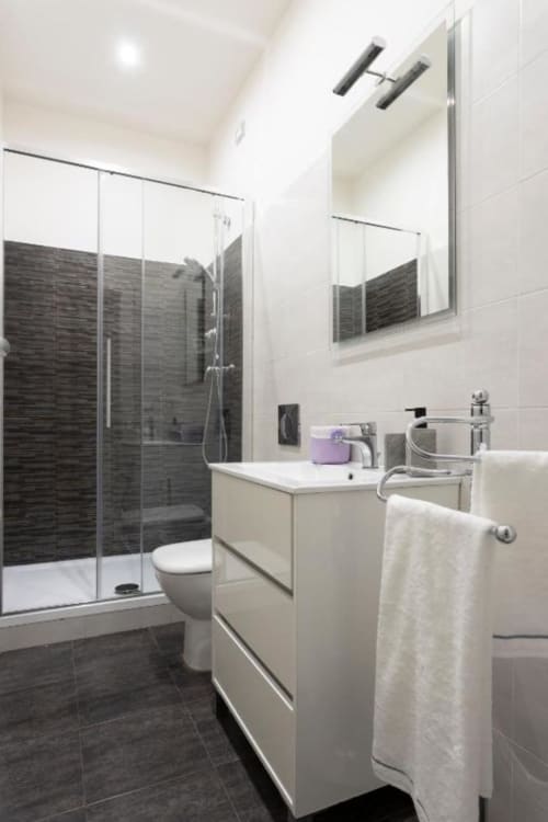 Bagno moderno all'Exclusive Domus Gaudia di Roma con doccia in piastrelle scure, lavabo bianco, specchio e finiture contemporanee