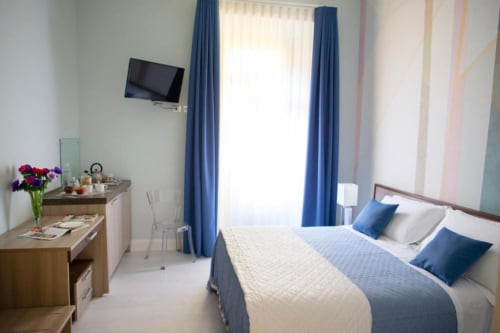 Elegante Suite Esecutiva a Domus Gaudia Roma con tende blu, letto matrimoniale, TV e vista città