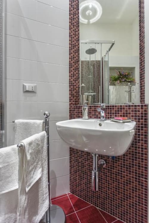 Bagno moderno della villetta Pia Domus presso Exclusive Domus Gaudia Roma, con lavabo bianco, piastrelle mosaico bordeaux e
