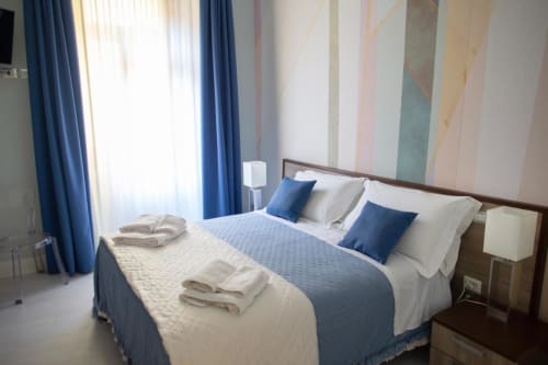 Camera moderna presso Domus Gaudia Roma con letto matrimoniale, accenti blu, arte murale a righe e luce naturale dalle ampie finestre