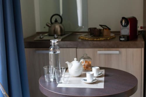 Suite moderna all'Hotel Domus Gaudia Roma con tavolo rotondo, teiera bianca, bicchieri e angolo cottura sullo sfondo