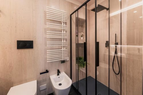 Bagno moderno a Domus Gaudia Roma con pareti in marmo beige, doccia con cornice nera, lavabo bianco, scaldasalviette e