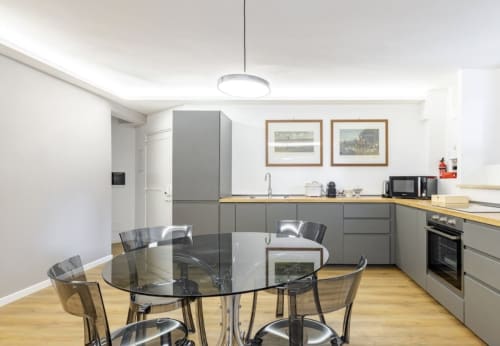 Modern Rome apartment kitchen and dining area with gray cabinetry, wooden counters, glass dining table, and stainless steel