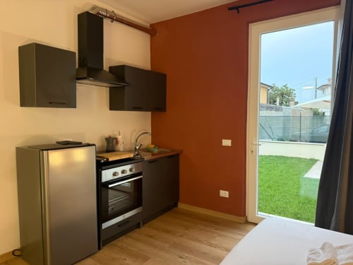 Moderna cucina con elettrodomestici neri, parete arancione e porta-finestra che si affaccia sul giardino a Mistral Holidays, Marina di