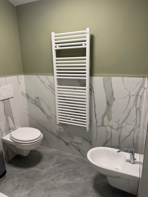 Bagno moderno con scaldasalviette bianco, rivestimento effetto marmo, lavabo a parete e toilette dell'appartamento Mistral Holidays