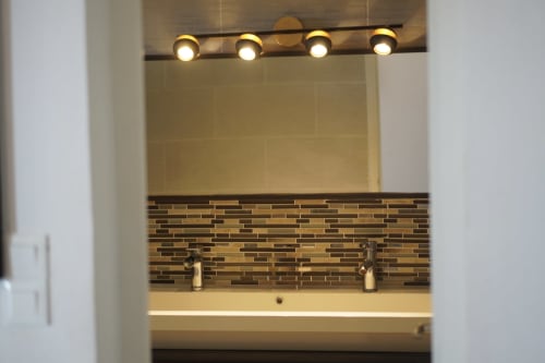 Modern bathroom sink with dual faucets, striped tile backsplash, and four round vanity lights at Kaz Kafe in Mamoudzou
