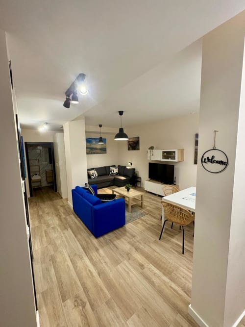 Sala de estar moderna en Ruzafa, Valencia con sillón azul, sofá oscuro, suelo de madera y zona de comedor
