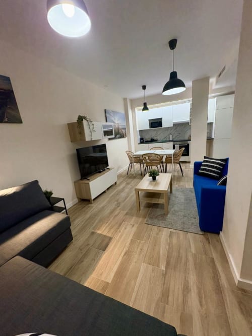 Salón moderno de apartamento en el barrio de Ruzafa, Valencia, con sillón azul, suelos de madera y lámparas colgantes negras
