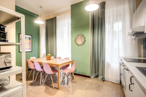 Moderna zona cucina-soggiorno in appartamento color verde Borghese a Roma, con sedie rosa e tavolo in legno