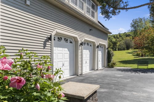 Modern garage with three white doors at Malkita Homes in Highland Mills, landscaped with pink flowers