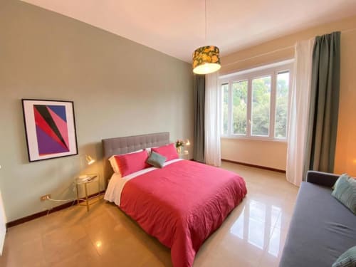 Camera da letto moderna con biancheria rosa, testata grigia, vista giardino, lampada a sospensione e opere d'arte contemporanea in appartamento a Roma
