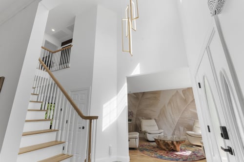 Modern foyer at Malkita Homes Highland Mills with wooden staircase, pendant lighting, and luxury bedroom suite visible