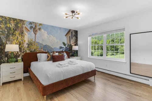 Spacious master bedroom at Malkita Homes with brown bed, large windows, tropical mural, and wood flooring
