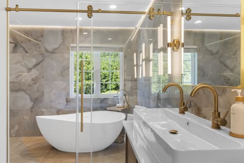 Modern luxury bathroom at Malkita Homes with marble walls, freestanding white tub, dual vanity, and gold fixtures.