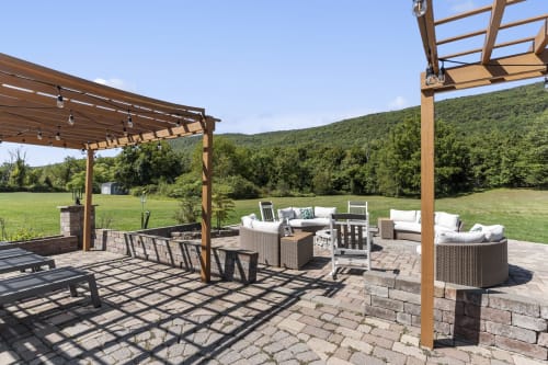 Luxe outdoor patio at Malkita Homes with wooden pergolas, wicker seating, fire pit, and mountain views in Highland Mills.