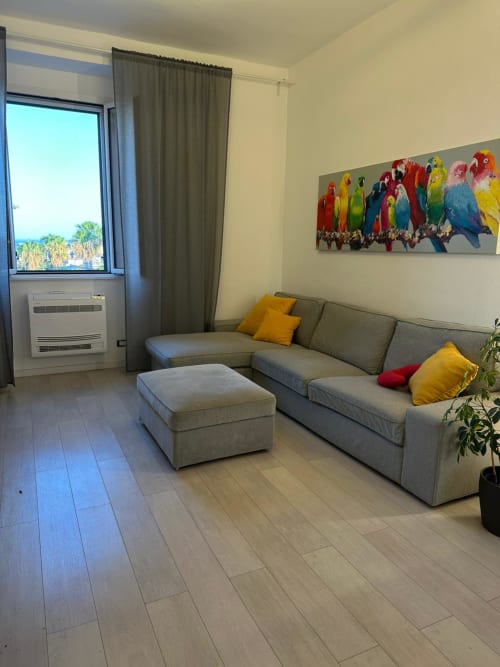 Bright modern apartment living room at Aparthotel Bentivoglio Catania with gray sofa, colorful parrot artwork, sea views