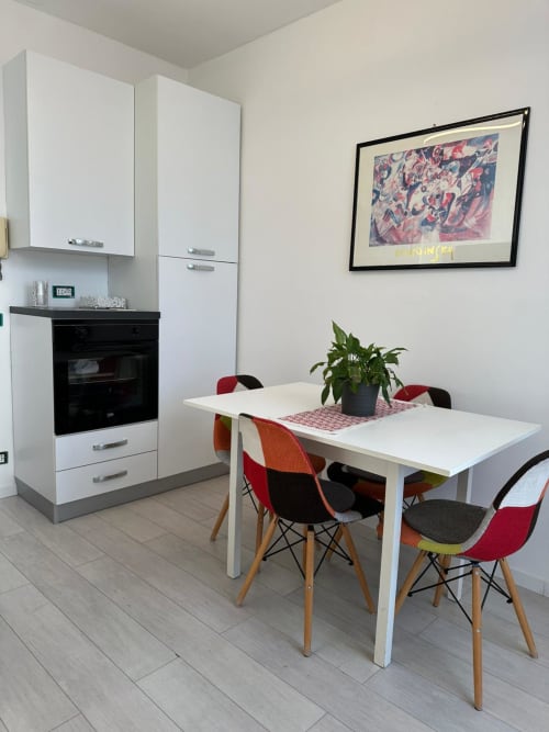 Modern kitchen-dining area in ApartHotel Lumi, Catania with white cabinetry, dining table, and colorful chairs