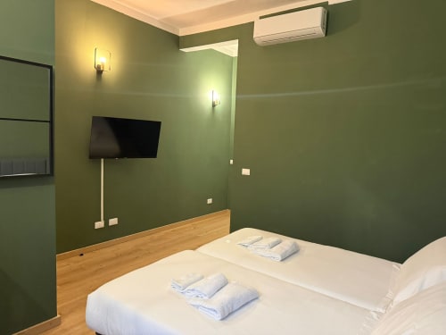 Modern bedroom at Mistral Holidays Marina di Carrara with green walls, wood headboard, TV, AC unit, and white bedding