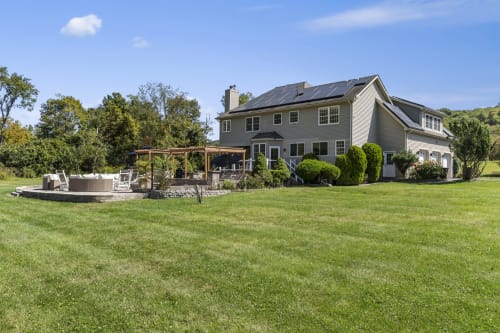 Modern farmhouse with solar panels, expansive lawn, fire pit, and pergola in Highland Mills