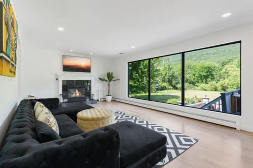 Modern living room at Malkita Homes in Highland Mills with black sectional, fireplace, and expansive views of forested