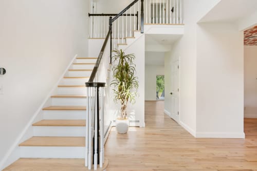 Modern staircase with wooden treads and metal railing in Highland Mills home entry, white walls, potted plant