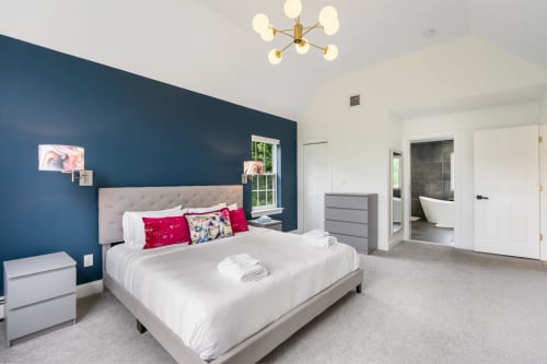 Modern bedroom at Malkita Homes with deep blue accent wall, queen bed, and ensuite bathroom in Highland Mills.