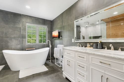Modern luxury bathroom at Malkita Homes Highland Mills with freestanding tub, white vanity, gray tile, and skylight window.