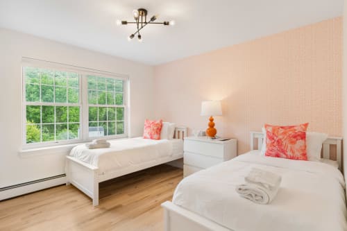 Bright bedroom at Malkita Homes in Highland Mills with twin beds, pink wallpaper, large windows, and modern furnishings.