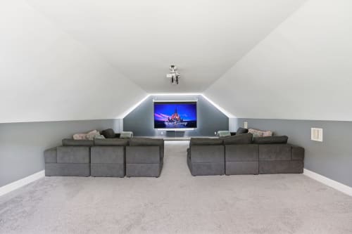 Modern attic media room at Malkita Homes with two gray sectional sofas facing a wall-mounted TV displaying Disney logo in
