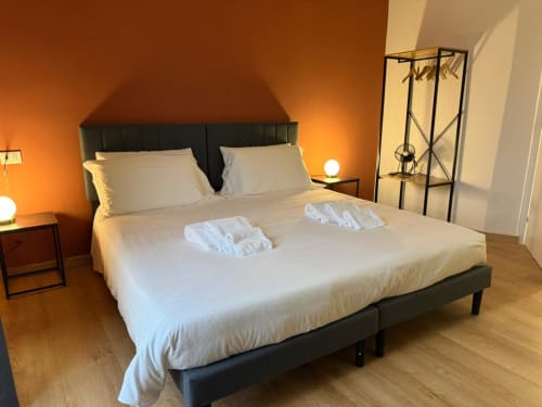 Camera da letto moderna con letto a baldacchino nero, biancheria bianca, parete accent arancione e pavimento in legno presso Mistral Holidays Marina di Carrara