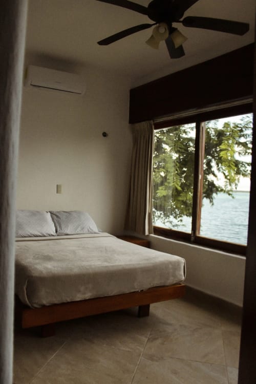 Dormitorio en villa Tucan Village de Bacalar con cama, ventilador de techo y vista al lago a través de puertas de vidrio
