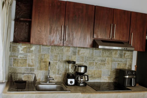 Cocina moderna en villa Tucan Village, Bacalar con gabinetes de madera oscura, salpicadero de azulejos, electrodomésticos de acero inoxidable y vista al lago