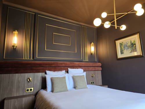 Modern bedroom at Le Castel B&B in Bayeux with gold-accented wall paneling, white bedding, and elegant lighting