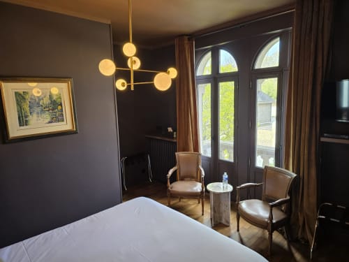 Elegant Chambre Balcon at Le Castel Bayeux with modern gold chandelier, neutral furnishings, and cathedral city views