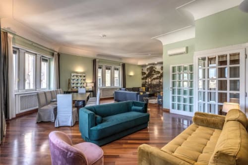 Ampio soggiorno panoramico della penthouse Imperial a Roma con parquet, divano teal, pareti verdi e arredi moderni