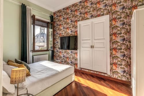 Elegante camera da letto in attico romano con carta da parati floreale, pavimenti in legno, ante armadio bianche e vista su monumento cupola