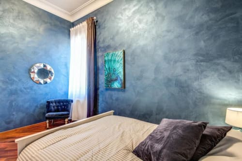Camera da letto moderna in appartamento romano con pareti azzurre texture, pavimento in legno, cuscini neri e opere d'arte decorativa